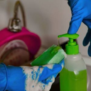Close-up of hands in rubber gloves holding a sponge and squeezing out dishwashing liquid. Green detergent.